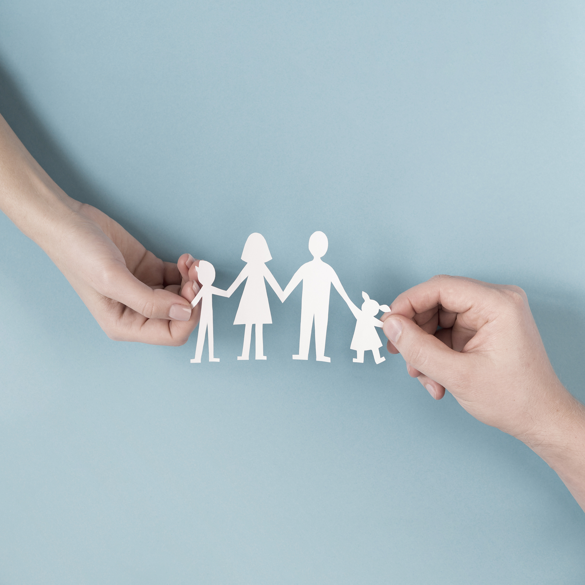 two hands holding a paper-cut family figure in front of light blue background